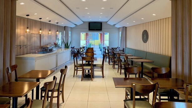 A modern restaurant interior with wooden panel walls, a central bar area, and multiple seating options including tables and booths. - Kanoa Hotel (Santo Antônio da Platina)