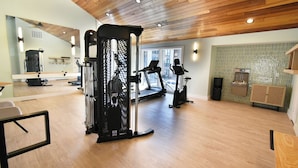 Un gimnasio con equipo de ejercicio, cinta de correr y pared espejada.
