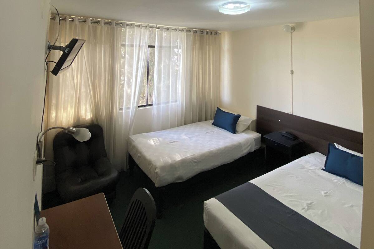 Une chambre d’hôtel avec un lit, un bureau, une chaise et une fenêtre avec des rideaux.