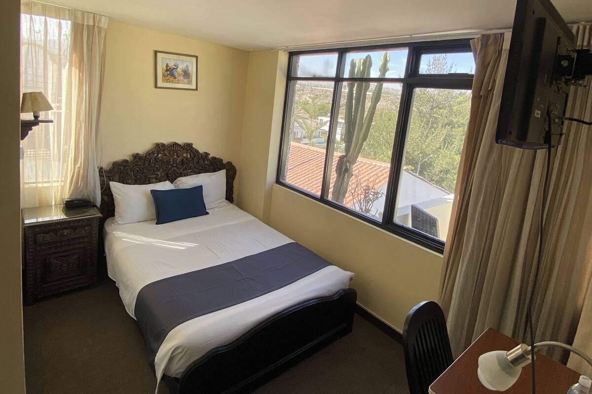 Une chambre d’hôtel équipée d’un lit, d’un bureau, d’une chaise, d’une télévision, d’une fenêtre donnant sur un paysage agréable et d’un luminaire au plafond.