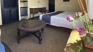 A bedroom with a bed, a round table, a TV, a desk, and a potted plant.