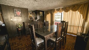 A dining area with a wooden parquet floor, a glass-top table, and ornate chairs.