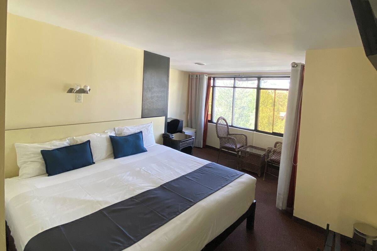 Une chambre d’hôtel avec un grand lit, un bureau, une chaise et une fenêtre avec des rideaux.