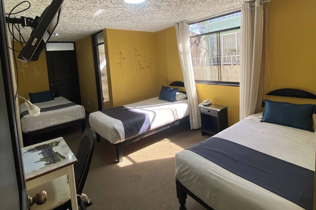 Une chambre d’hôtel avec deux lits, un bureau, une chaise, un plafond orné d’un motif texturé et une fenêtre avec des rideaux.