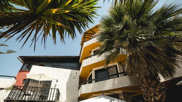 A multi-story building with balconies, outdoor seating, and palm trees.