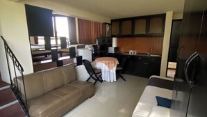 A modern living room with a sofa, a dining table, and a kitchen area with cabinets and a sink.