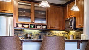 A kitchen with wooden cabinets, a stone backsplash, and pendant lighting. - Mountain Luxe (Canmore)