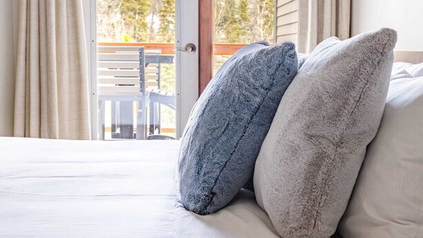 A bedroom with a bed, two pillows, and a view of a mountain landscape through a door. - Mountain Luxe (Canmore)