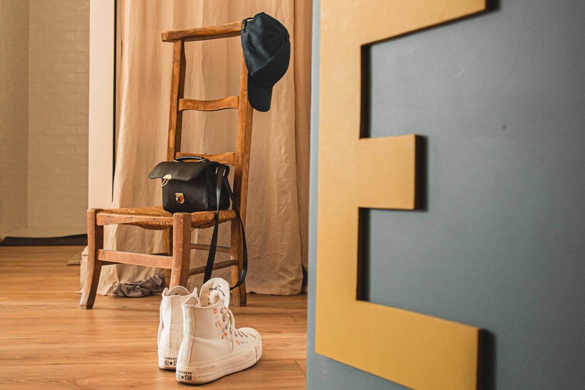 A wooden chair with a black bag and white sneakers on a wooden floor.
