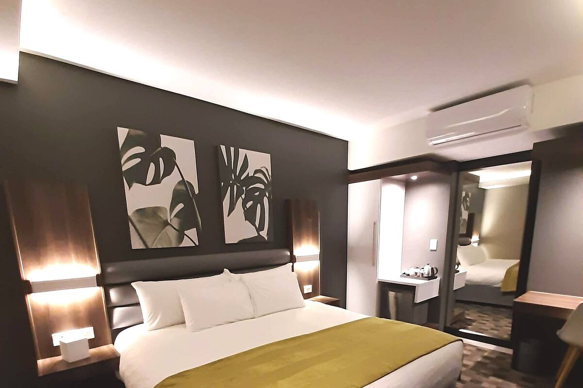 A modern hotel room with a large bed, a desk, and a mirror.