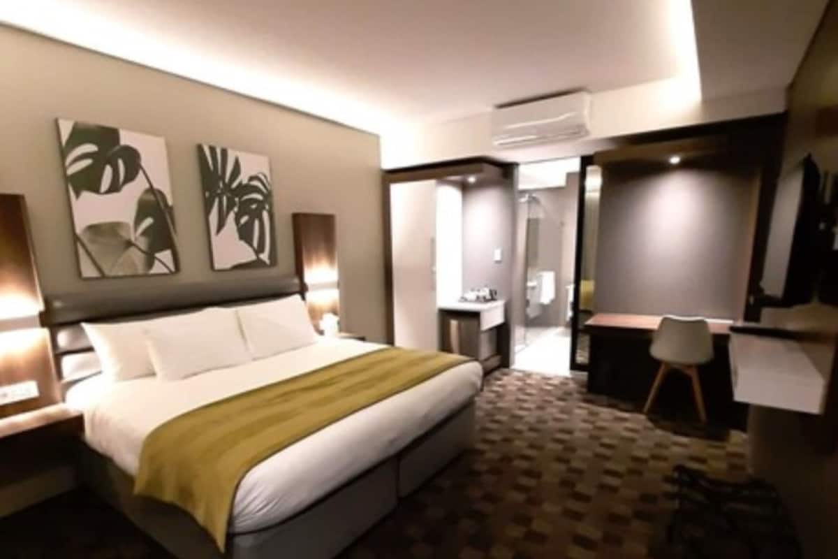 A modern hotel room with a large bed, a desk, and a chair. There are two wall-mounted air conditioning units and a mirror.