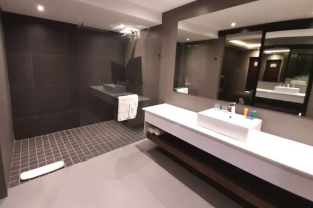 A modern bathroom with a large mirror, a white vanity, and a shower area.