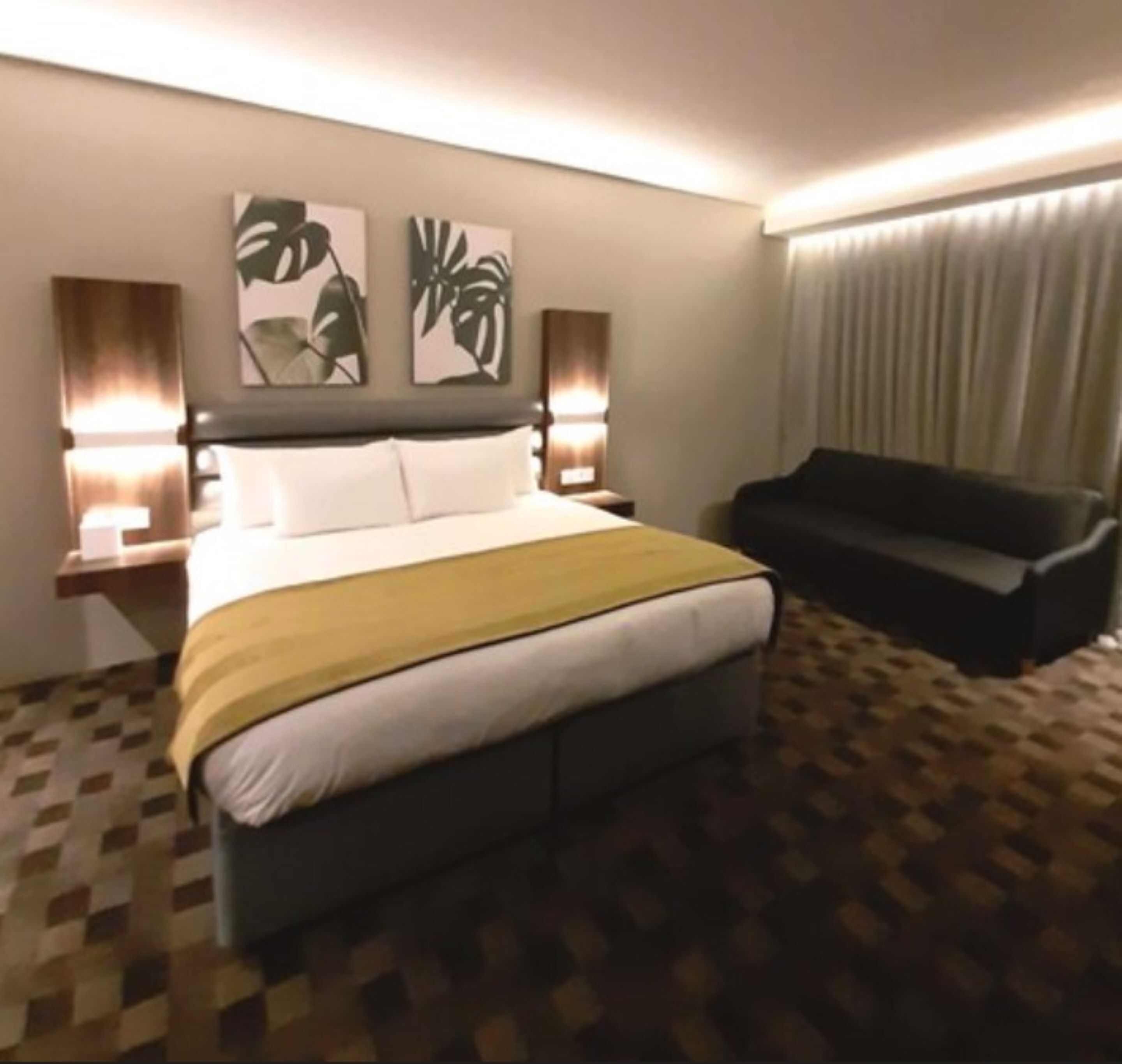 A hotel room with a large bed, two bedside tables with lamps, a sofa, and abstract wall art.