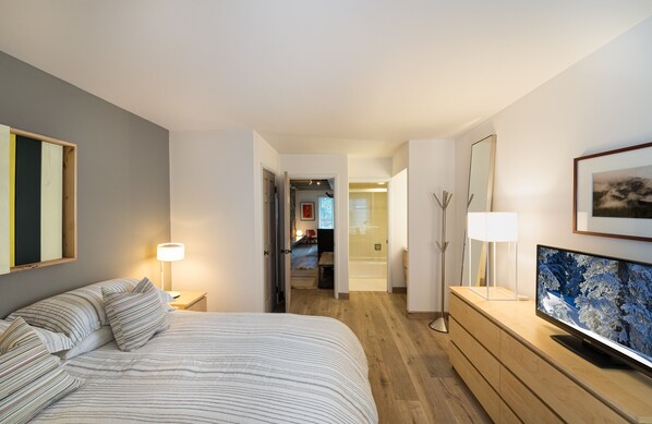 A hotel room with a bed, a TV on a wooden dresser, a mirror, and a door leading to another room. - Treetops 4D Lionshead Village (Vail)