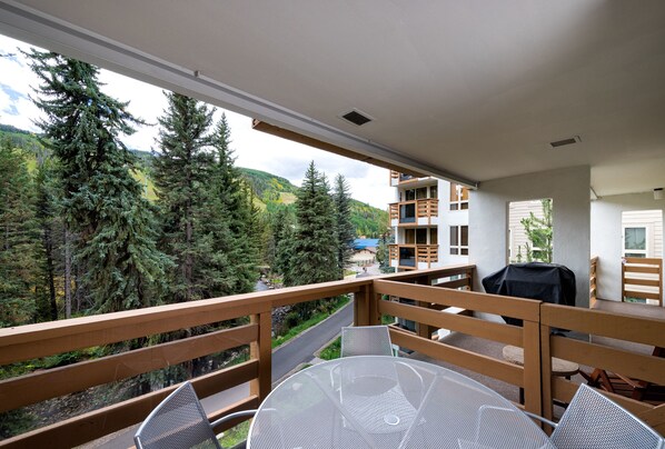 A balcony with a view of a forested area and a building in the background. - Treetops 4D Lionshead Village (Vail)