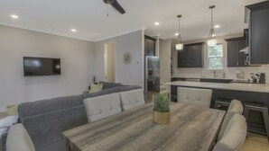 Un salon moderne avec un canapé gris, une table à manger en bois et un ventilateur de plafond.