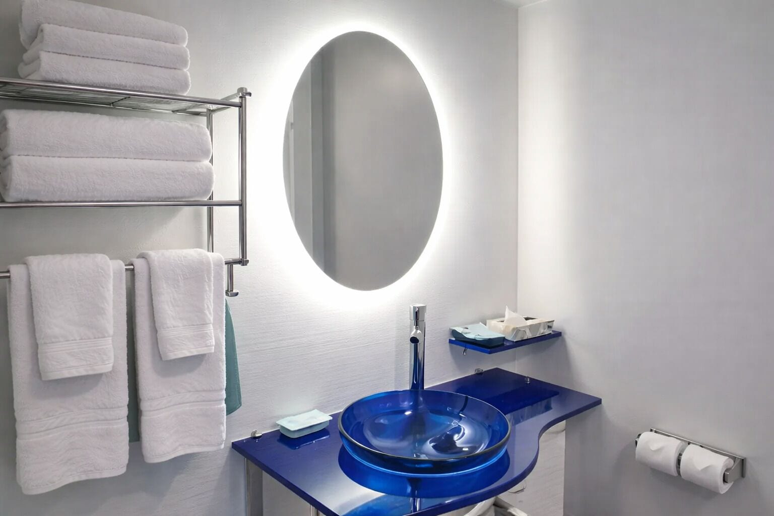 Uma casa de banho com uma pia azul, um espelho, um porta-toalhas com toalhas dobradas e um suporte de tecidos.