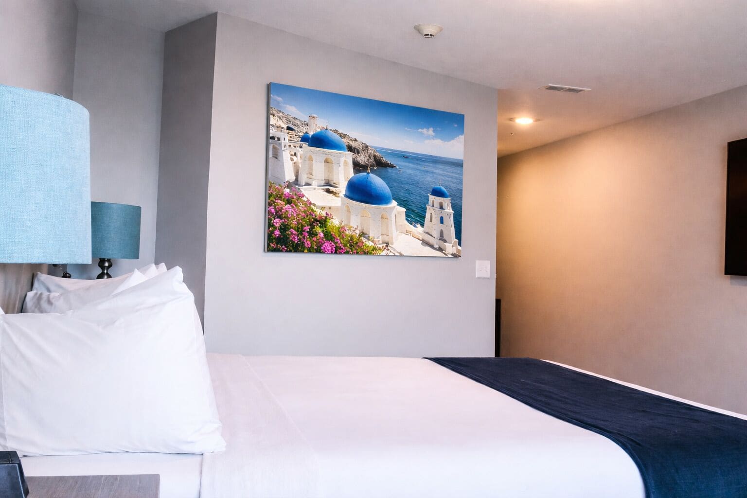 A hotel room with a bed, a wall-mounted lamp, and a painting of a coastal scene.