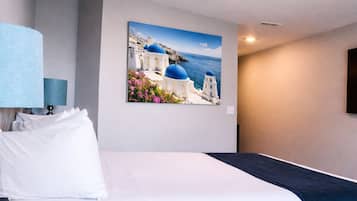 A hotel room with a bed, a wall-mounted lamp, and a painting of a coastal scene.