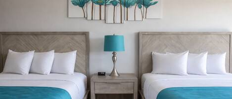 A hotel room with two beds, a nightstand with a lamp, and a wall-mounted artwork of flowers.