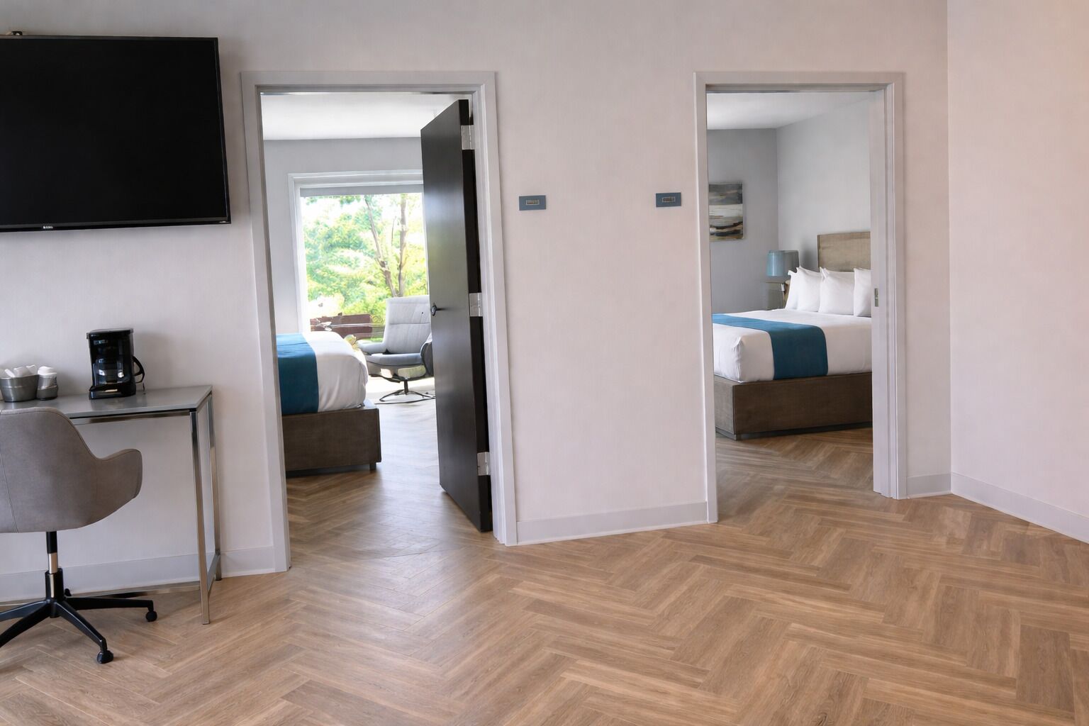 A hotel room with a bed, a desk with a coffee maker, a chair, and a TV.