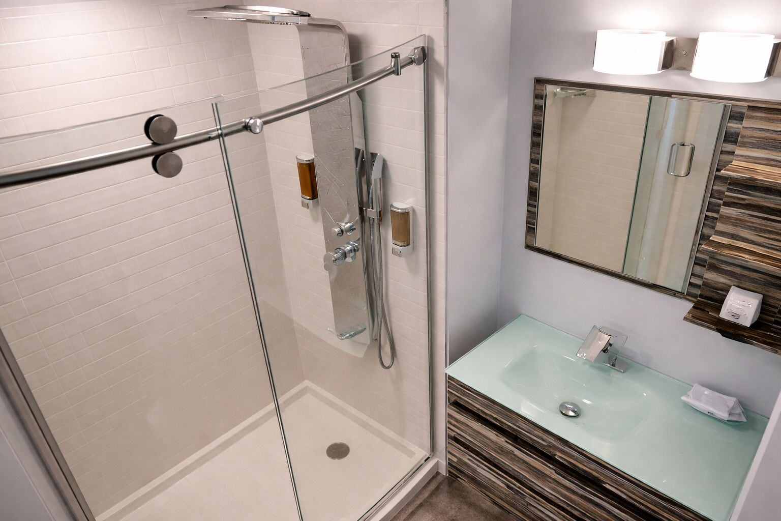 A modern bathroom with a glass shower enclosure, a glass sink, and a mirror with a wooden accent wall.