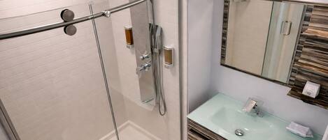 Une salle de bain moderne dotée d’une douche en verre, d’un lavabo en verre et d’un miroir agrémenté d’un mur d’accent en bois.