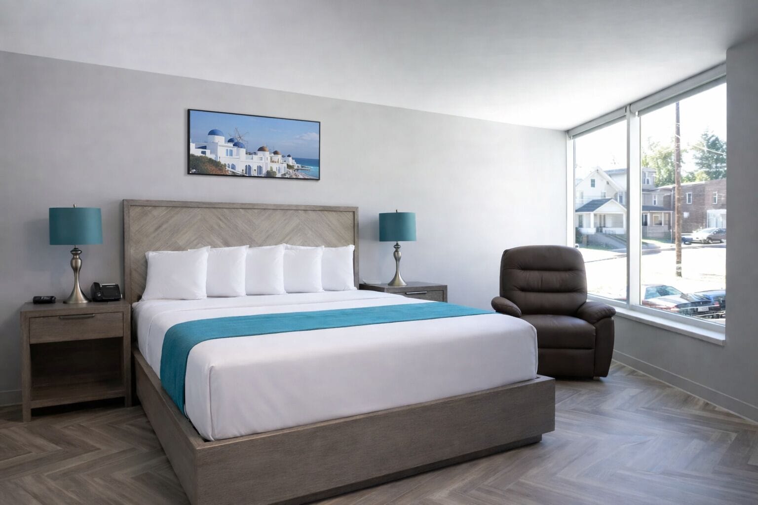 Ein Hotelzimmer mit einem großen Bett, zwei Nachttischen, einem Sessel, einem Fenster mit Aussicht und einem Bild an der Wand.