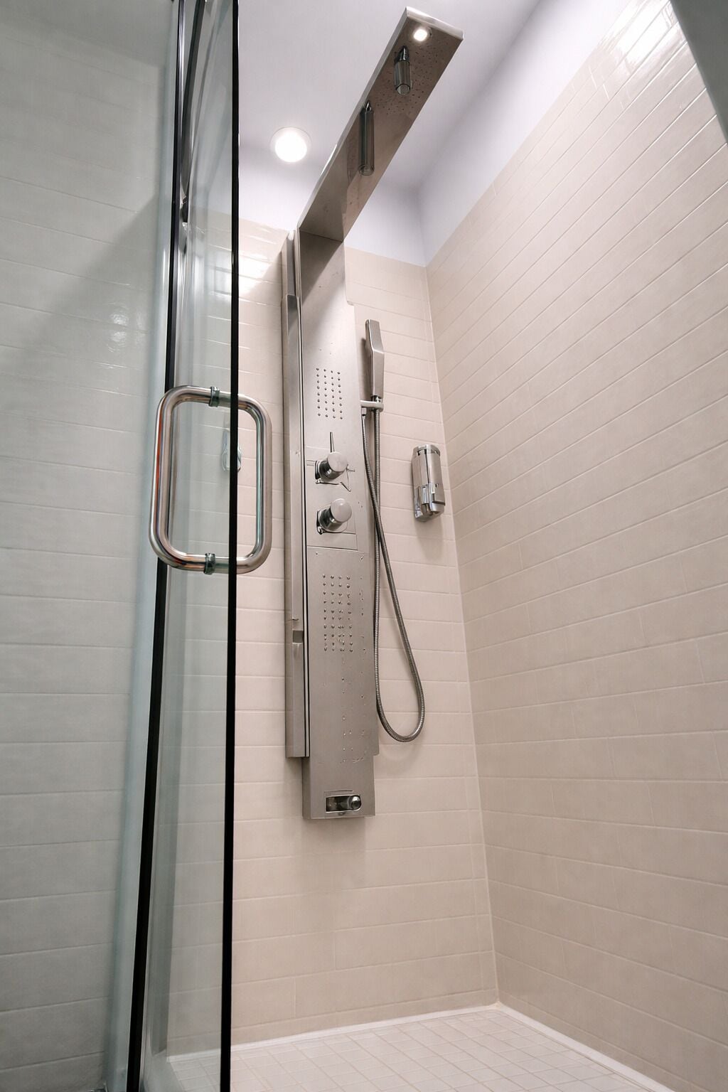 Una ducha moderna con cabina de vidrio, cabezal de ducha de mano y panel de control empotrado.