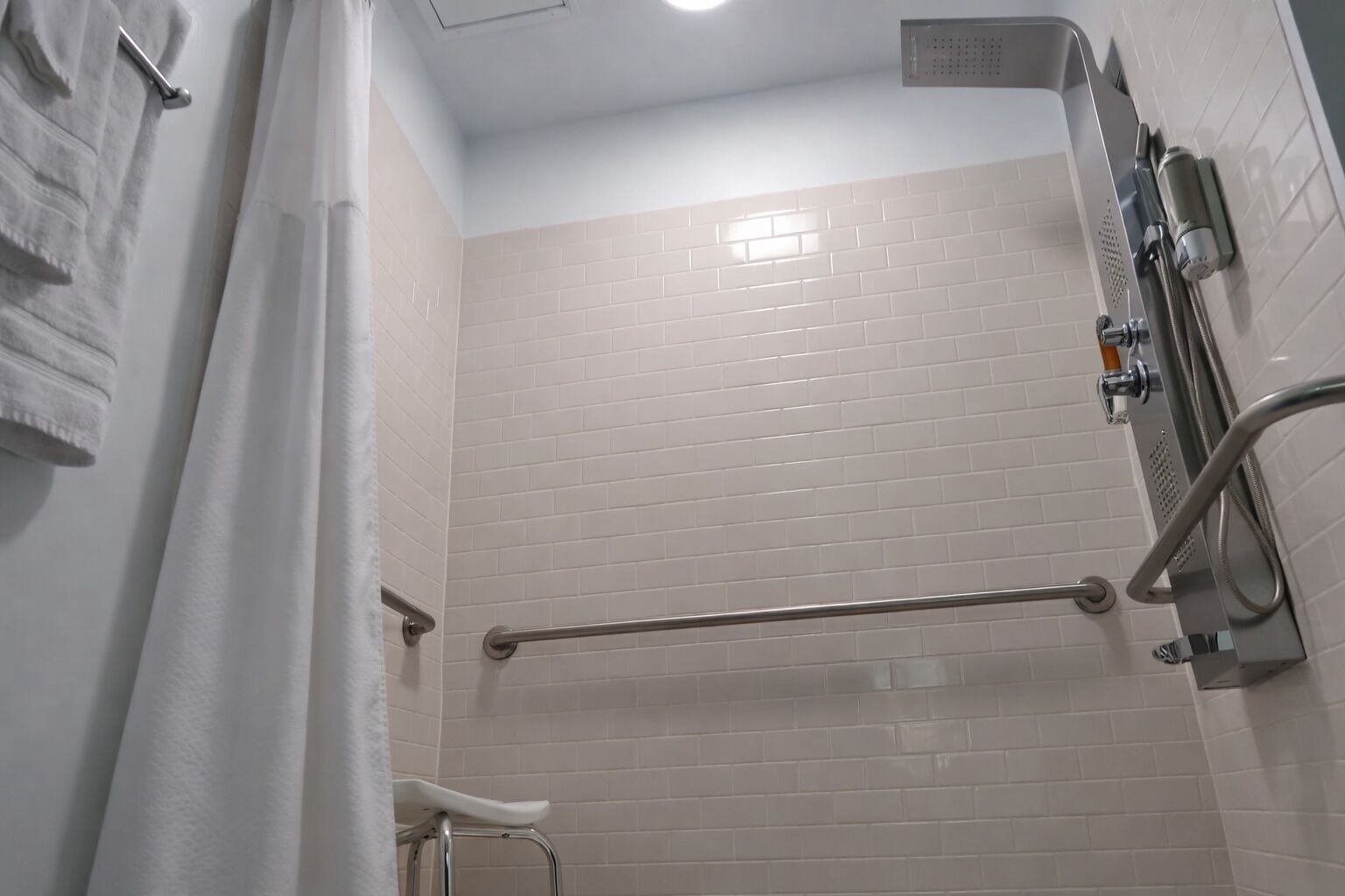 Een badkamer met witte betegelde wanden, een douche met handdouche, een handgreep en een handdoekrek.