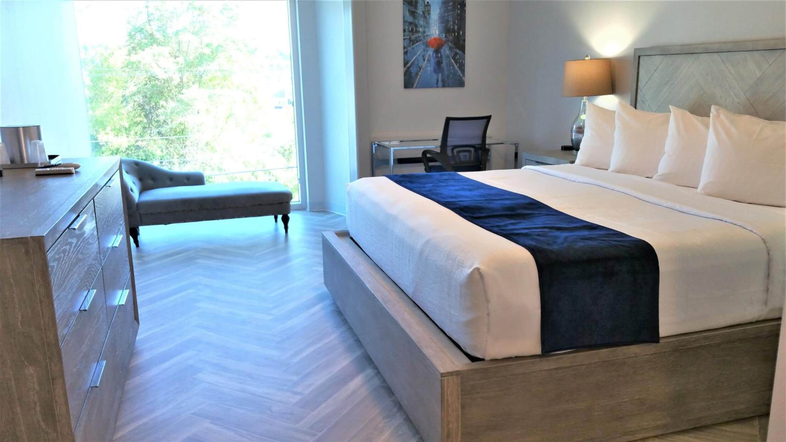 Ein Hotelzimmer mit einem großen Bett, einem Schreibtisch, einem Stuhl und Blick auf Bäume durch das Fenster.
