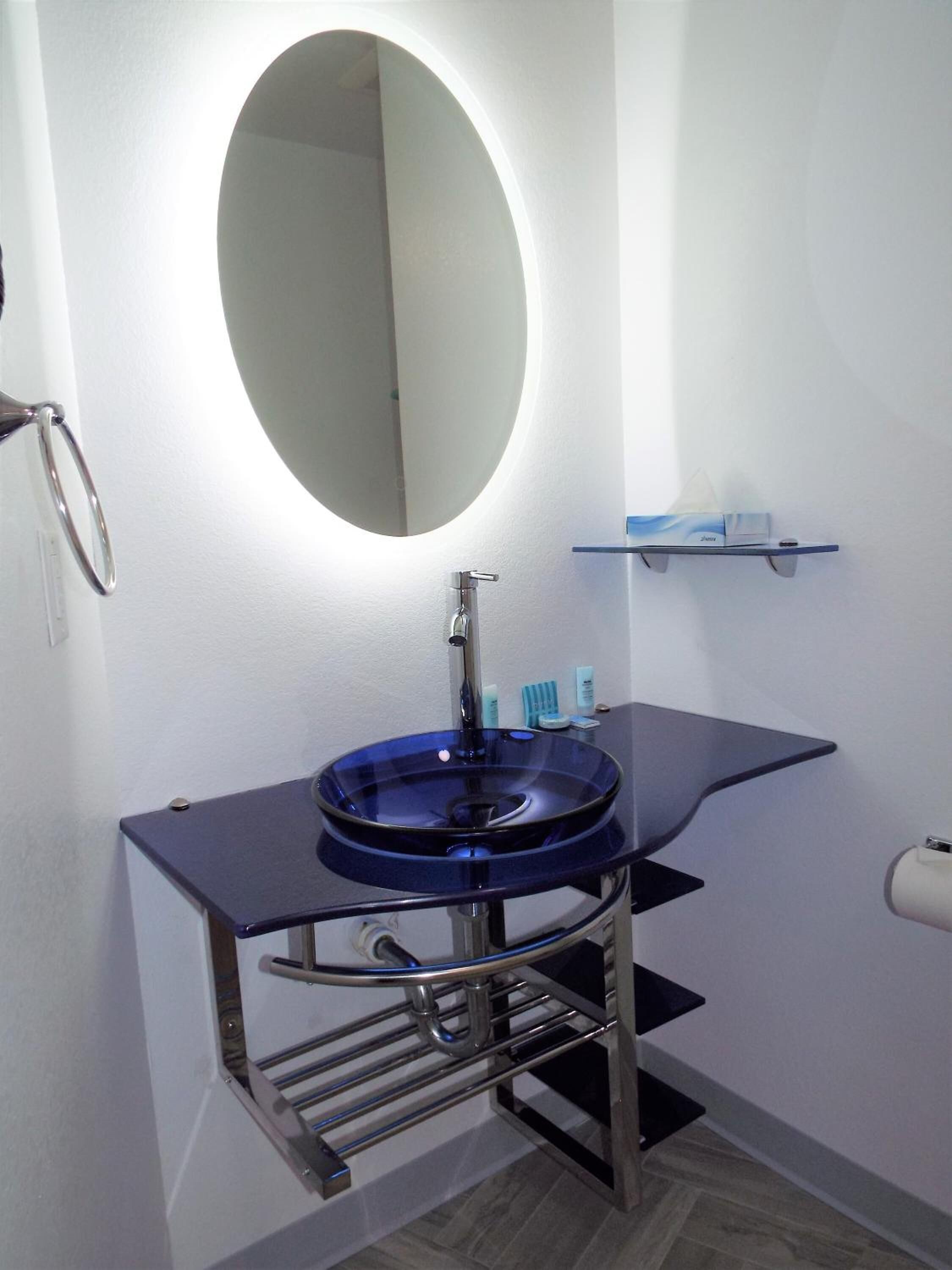 A bathroom with a round mirror, a blue sink, and a towel rack.