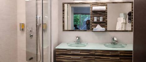 A modern bathroom with a glass-enclosed shower, two glass sinks, and a large mirror with a view of the outdoors.