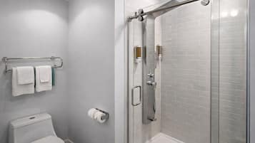 Ein Badezimmer mit Toilette, einer Duschkabine aus Glas und einem Handtuchhalter mit Handtüchern.