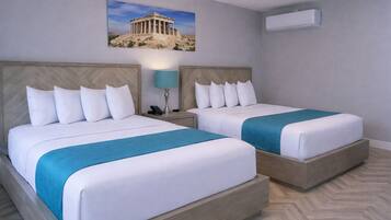 A hotel room with two beds, a nightstand with a lamp, a wall-mounted air conditioner, and a picture of the Parthenon.