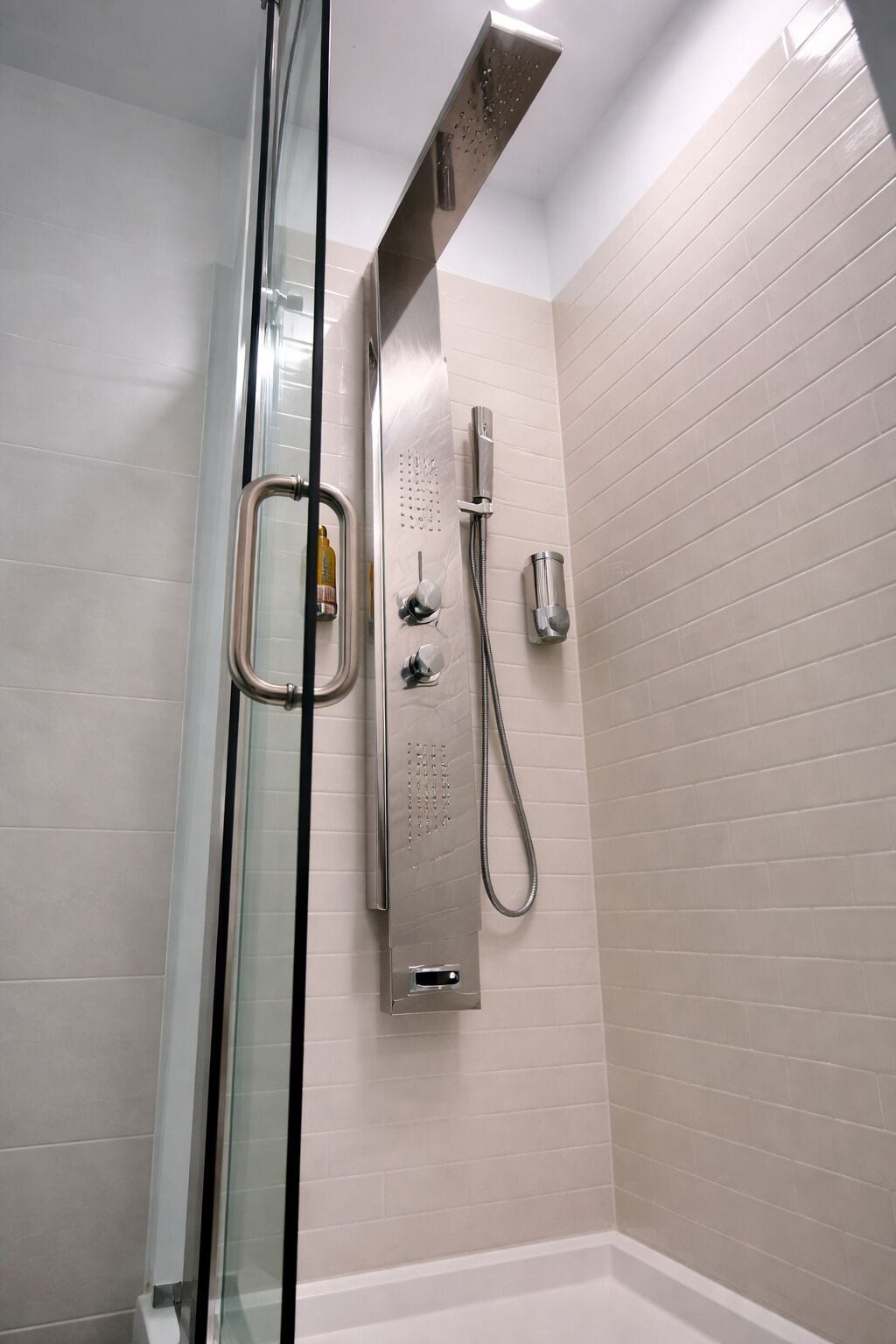 A modern shower with a glass enclosure, a handheld showerhead, and a wall-mounted control panel.