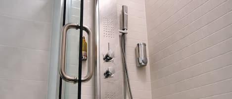 A modern shower with a glass enclosure, a handheld showerhead, and a wall-mounted control panel.