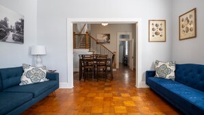 Een woonkamer met een blauwe bank, een eettafel met stoelen en een trap naar een bovenverdieping.
