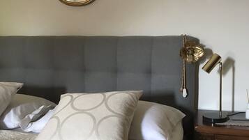 A neatly made bed with a grey headboard, a mirror above it, and a bedside table with a lamp and a small decorative item.
