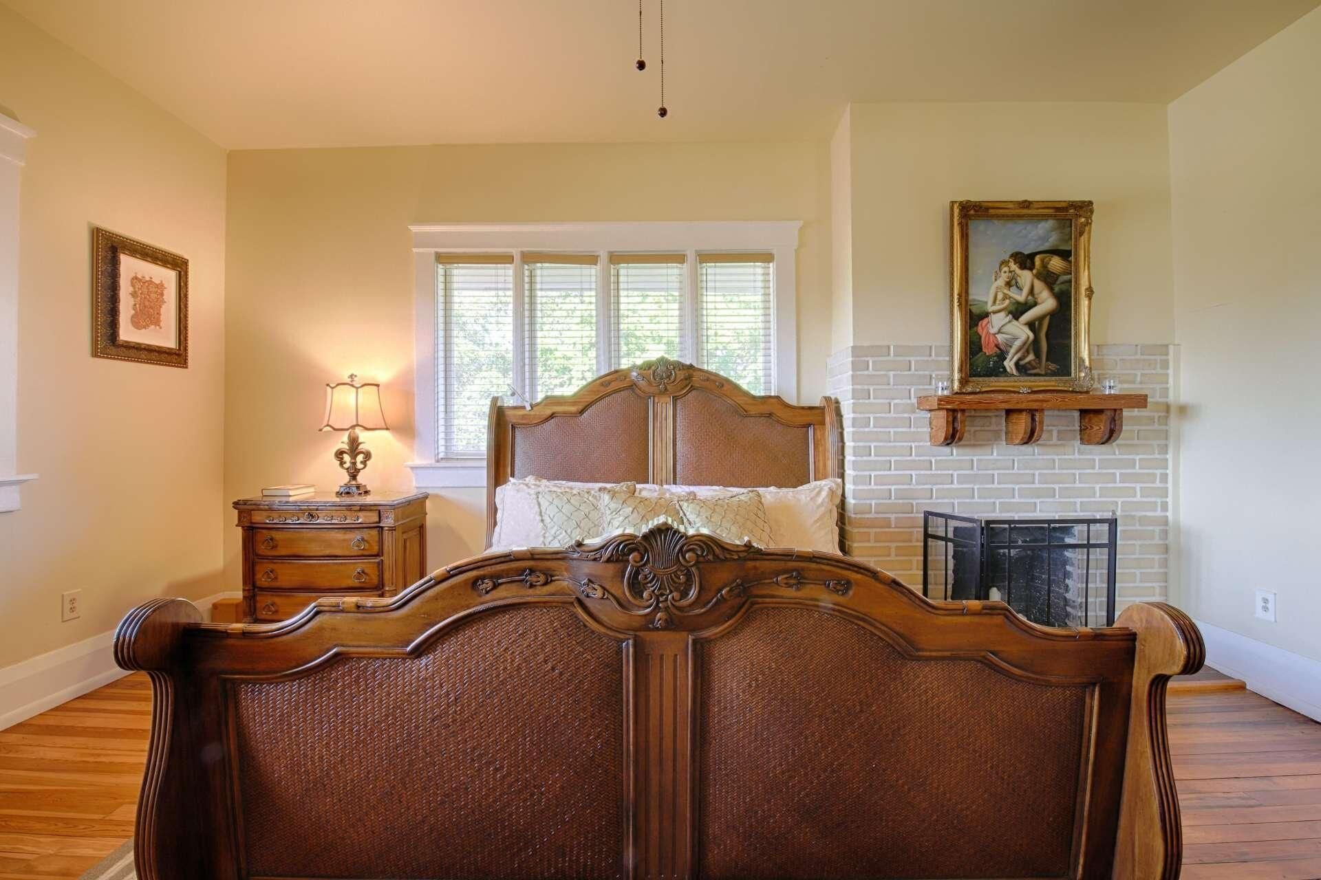 A bedroom with a wooden bed, a nightstand with a lamp, a fireplace, and a framed picture on the wall.
