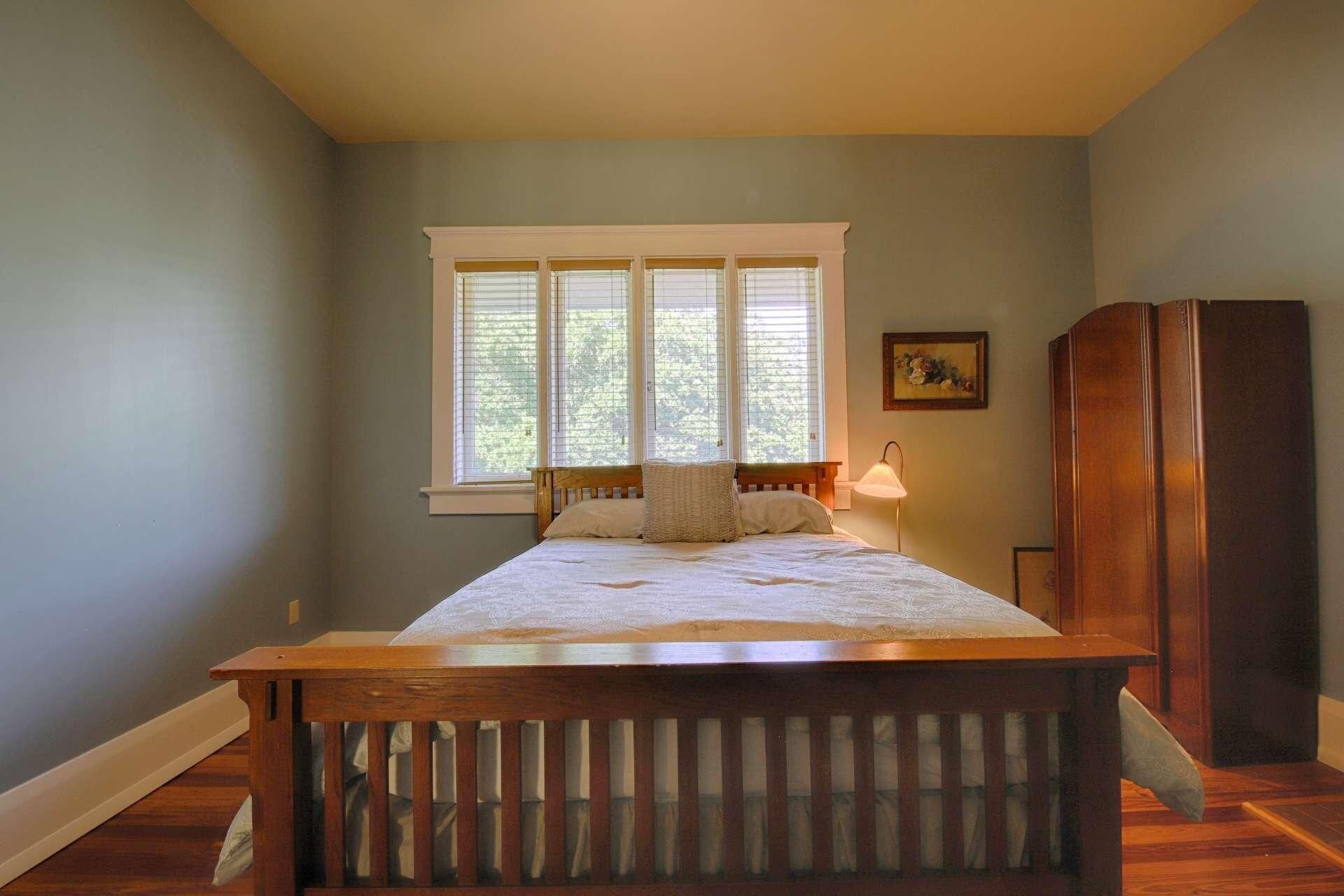 Une chambre à coucher avec un lit en bois, une fenêtre avec des stores, une lampe de chevet et une armoire en bois.