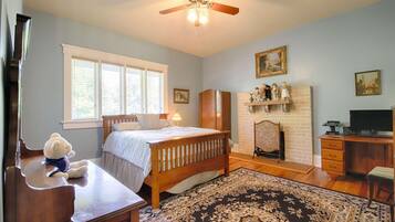 A bedroom with a bed, a dresser, a desk, a chair, a fireplace, and a ceiling fan.