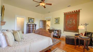 A spacious bedroom with a large bed, a wooden dresser, a desk, and a chair. There is a ceiling fan, a tapestry, and a bookshelf.