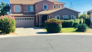 A two-story house with a tiled roof, a garage, and a well-maintained front yard with flowering bushes and a small tree.