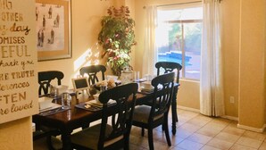 A dining area with a chandelier, a table set for four, and a large window with curtains.
