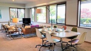 A modern dining area with a round table, white chairs, and a television in the background. - Gig Harbor- Secluded Apartment with Million Dollar View.  10-minute walk to town (Gig Harbor)