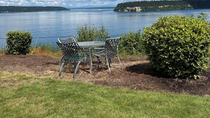 A lakeside view with a table and chairs, a bush, and a distant shoreline. - Gig Harbor- Secluded Apartment with Million Dollar View.  10-minute walk to town (Gig Harbor)