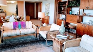 A living room with wicker furniture, a dining area with a table and chairs, and a bookshelf with various items. - Gig Harbor- Secluded Apartment with Million Dollar View.  10-minute walk to town (Gig Harbor)