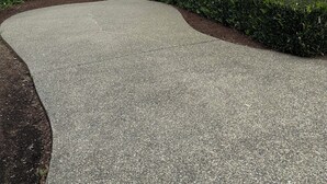 A modern building with a curved driveway leading to a gated entrance, a surveillance camera, and a view of a lake. - Gig Harbor- Secluded Apartment with Million Dollar View.  10-minute walk to town (Gig Harbor)