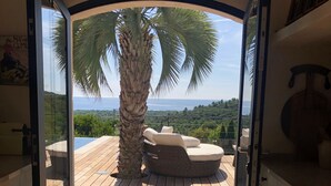 An open doorway leading to a balcony with a view of the sea, a palm tree, and a seating area. - Atmospheric villa with nice sea view in a quiet green area (La Croix-Valmer)